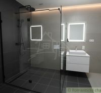 A bathroom in a family house with a glass shower enclosure and backlit mirrors.