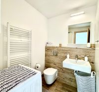 Bathroom in a studio apartment with a mirror, washing machine, and sink with wooden decor.