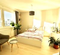 A bright room in a one-room apartment with a bed and a wooden decor floor.