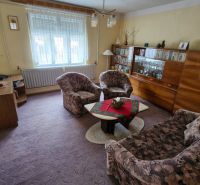 Living room in a family house with carpeted floor, furniture, and decorations on the shelves.