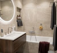 Bathroom with a bathtub, wall-mounted sink, and round illuminated mirror in a 2-room apartment.