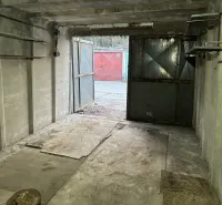Concrete garage with open steel doors, view of another garage outside.