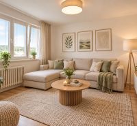 Living room in a two-room apartment with a sofa, plants, and wood-patterned flooring.