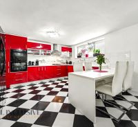 A kitchen in a family house with a black and white floor and red kitchen furniture.