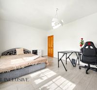 A room in a family house with a bed, table, and chair on a floor with a wooden decor.