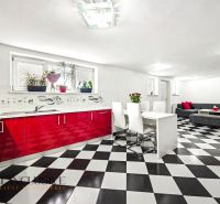 Bright kitchen and dining room in a family house with black and white tiles and red cabinets.