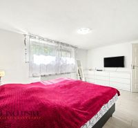 A bright bedroom with a red blanket, a TV on the wall, and a wooden decor floor.