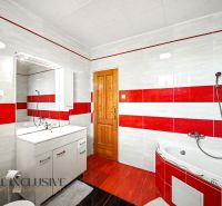 A family house bathroom with red and white tiles, a corner bathtub, and cabinets.