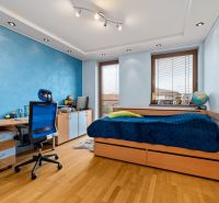 A children's room with a blue wall, a bed, a desk, and a wooden decor floor.