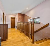 A hallway with a staircase in a family house, a floor with a wooden decor, a mirror, and plants.