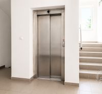 A hallway with an elevator and stairs leading to a window, 2-room apartment.