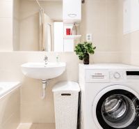 A bathroom in a 2-room apartment with a bathtub, washing machine, and sink.