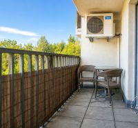 A balcony of a 2-room apartment with a view of greenery and seating furniture.
