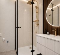 A bathroom in a 3-room apartment with an elegant shower, gold details, and a lighted mirror.