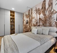 Bedroom in a two-room apartment with a wooden decor floor and wallpaper with an exotic motif.