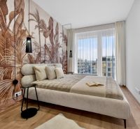 A bedroom in a 2-room apartment with tropical wallpaper and a wooden decor floor.