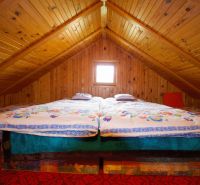 A cottage with wooden paneling has a double bed under a wooden ceiling.