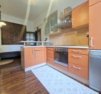 A kitchen in a 3-room apartment with a wooden decor floor and a brick wall.