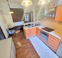 A kitchen with an orange cabinet, a sofa, and a wooden decor floor in a 3-room apartment.
