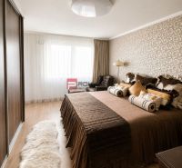 Bedroom in a 2-room apartment with wood-patterned flooring, a cozy bed, and patterned wallpaper.