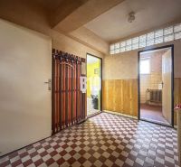 A hallway in a family house with wallpaper, a glass block window, and checkered tiles.