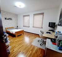 A room in a family house with a bed, a desk, and a wooden-patterned floor.