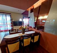 Dining area with flowers, a mirror, and a wooden-patterned floor in a family house.