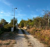 A reinforced dirt road leading to a cottage in Banka, lined with bushes and a fence.