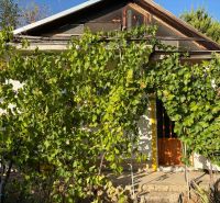 The cottage in the bank is covered with greenery and vine, the door is on a small wall.