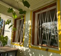 A window with a yellow frame and bars flooded with sunlight in a cottage in Banka.