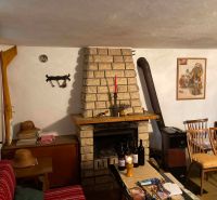 A room in a cottage with a fireplace, wooden chairs, and several bottles of wine on the table.