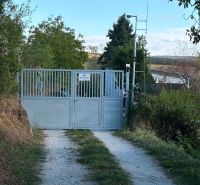 The gate leading to the cottage in Banka surrounded by greenery and a dirt road.