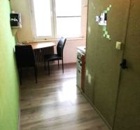 A kitchen in a studio apartment with wooden floor decor and a table by the window.