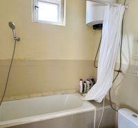 Bathroom with a bathtub, shower, boiler, and wooden decor flooring in a family house.