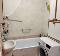 A bathroom in a studio apartment with a bathtub and a washing machine, tiled with light tiles.