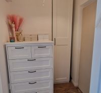 A room in a one-bedroom apartment with a chest of drawers, a wardrobe, and a floor with a wooden decor.