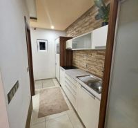 A narrow kitchen in a studio apartment with white cabinets and decorative tiles.