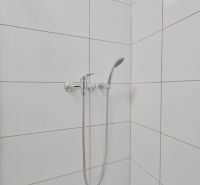 A shower corner with white tiles and a showerhead in a studio apartment.