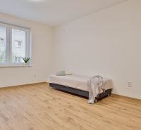 Studio apartment with a bed, wood-patterned floor, and a window with a view.