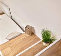 A studio apartment with a wooden floor, a bed, and a potted plant.