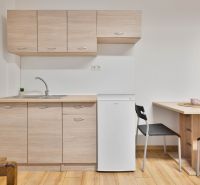 A kitchenette in a studio apartment with a white refrigerator and a wooden decor floor.