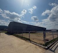 Building in Hniezdne, fenced area with horses, sunny sky, partly cloudy.