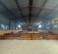 The interior of a building with wooden benches and a sandy floor, designed for events.