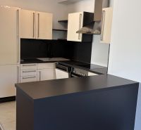 A kitchen in a 3-room apartment with an elegant black countertop and light cabinets.