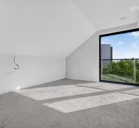 A room with a large window and gray flooring in a multi-room apartment.