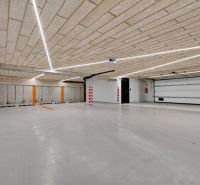 Parking garage with a concrete ceiling and floor, illuminated by linear lights.