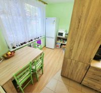 A kitchen in a 4-room apartment with a table, green chairs, and a floor with a wooden decor.