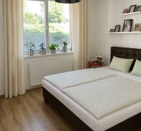 A bedroom with wood-patterned flooring, a large window, and a simple bed in a three-room apartment.