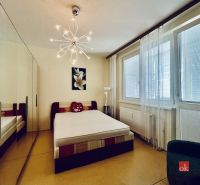 A studio apartment bedroom with a mirrored wardrobe, a bed, and large windows.