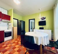 A kitchen in a studio apartment with colorful tiles, red cabinets, and a round table.